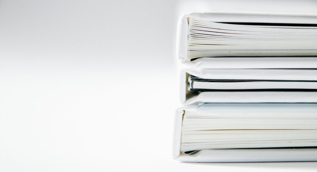 3 white binders filled with white paper stacked on top of each other on the right side of the photo with a white background